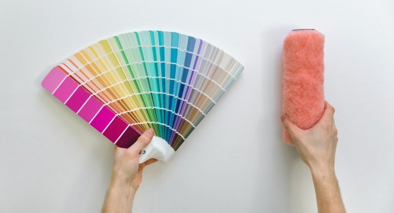 Échantillons de couleurs en éventail et rouleau de peinture tenus en mains