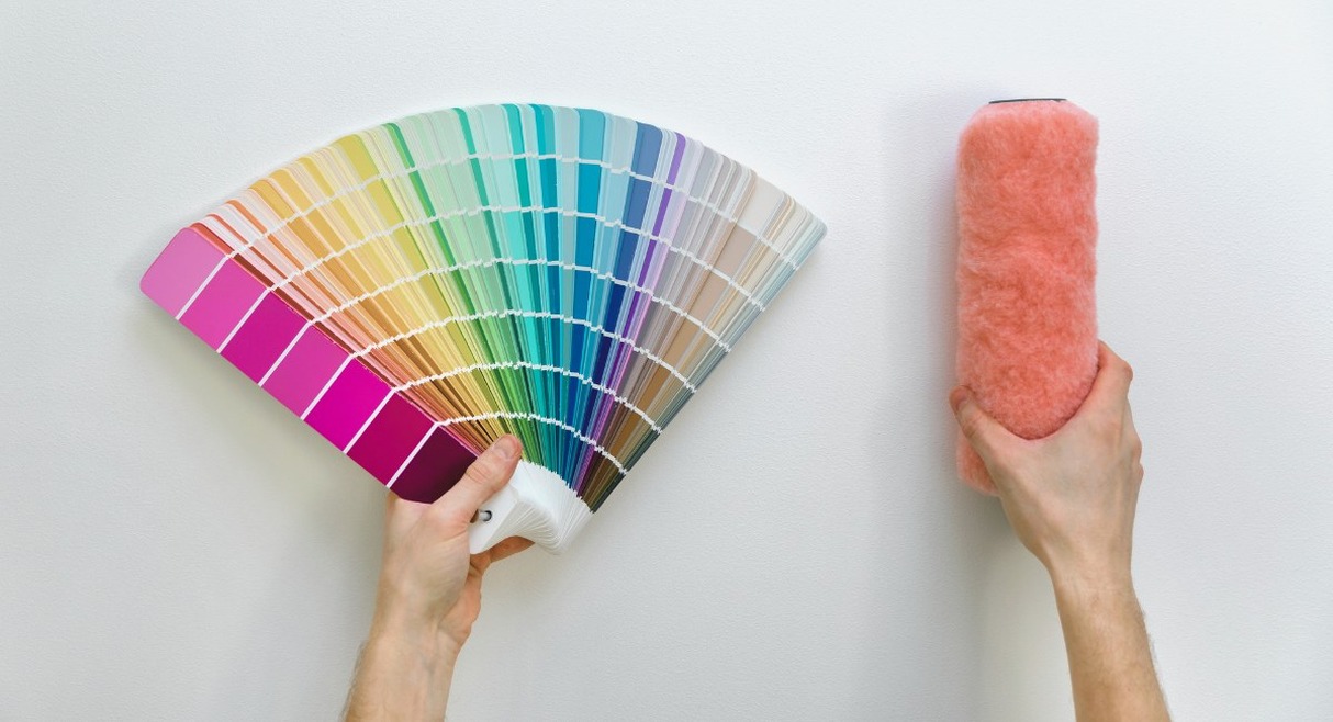 Échantillons de couleurs en éventail et rouleau de peinture tenus en mains