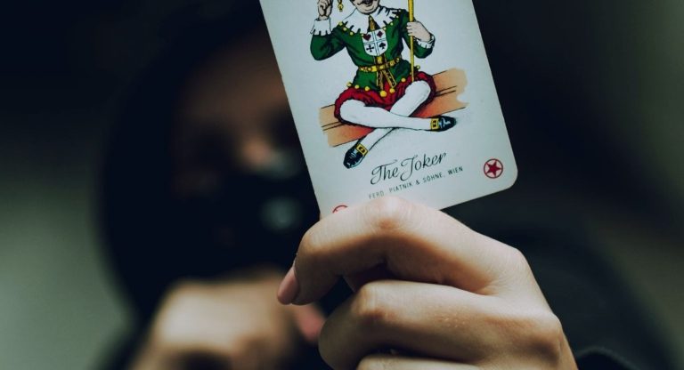 Silhouette encapuchonnée tenant une carte à jouer Joker dans l'ombre