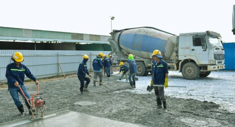 Ouvriers coulant et lissant une dalle de béton avec camion toupie
