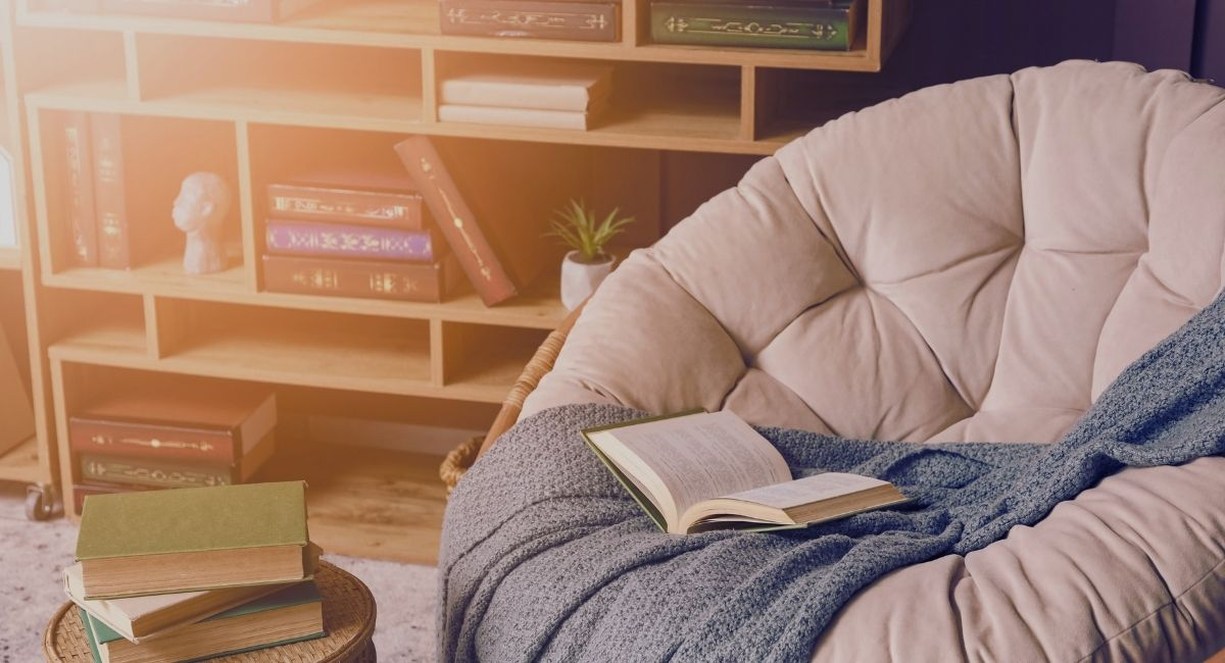 Livre ouvert posé sur un fauteuil douillet devant une bibliothèque